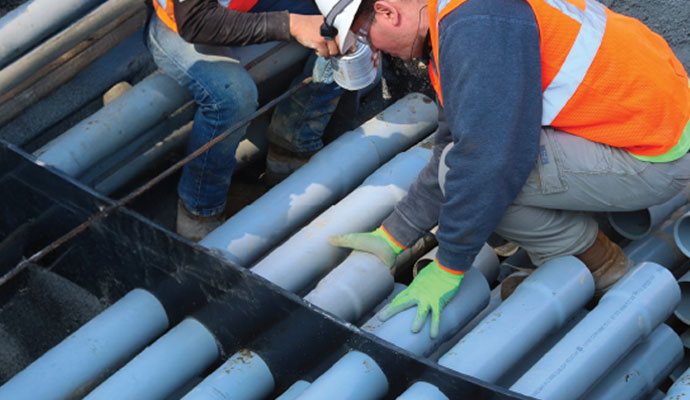 Workers Installing Utility Conduits in a Duct Bank Two construction workers installing and aligning gray utility conduits in a duct bank frame.